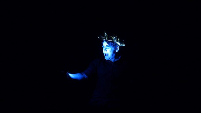 Schauspieler sieht sich selbst in blauem Licht vor schwarzem Hintergrund.