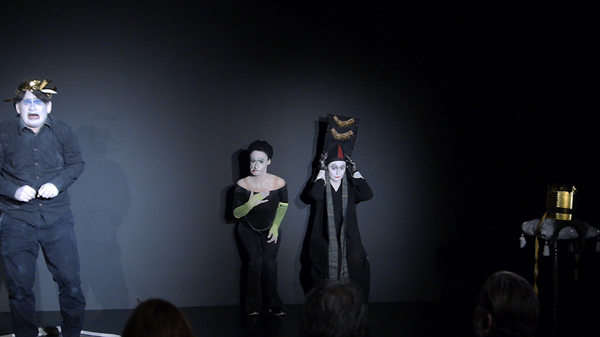 Drei Schauspieler stehen auf der Bühne. der ganz rechte scheint zu weinen, die in der Mitte verzieht ihren Mund und die ganz linke hält ihren Hut mit beiden Händen fest.