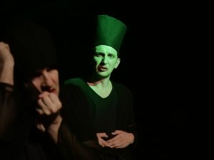 Probenfoto Wandlung21: Zwei Schauspieler im grün beleuchtetem Bühnenraum. Sie zwigen starke Gebärden im Profil.