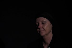 Eine Frau mit geschlossenen Augen vor schwarzem Hintergrund.
