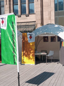 Unser Stand auf der Ehrenamtsmesse 2023. Vorne linka unsere grüne Beachflag, im Zelt hängen drei große Theaterfotos