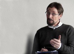 Wolfgang Keuter spricht über Slow Acting. Er sitzt auf einem Stuhl mit einem freundlichen, konzentriertem Gesichtsausdruck.