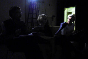 Im schwarzen Bühnenraum diskutieren die Spieler über den Text von Leonce und Lena. Im Hintgergrund die offene Tür.
