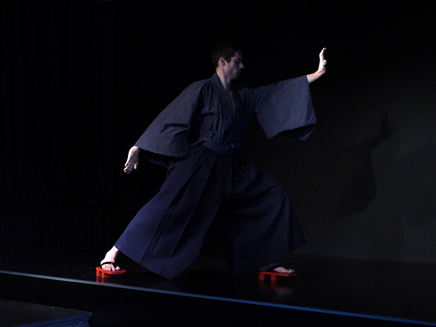 Ein junger Mann, Hisashi, steht in einem Karatestand. Er trägt einen blauen Kimono und eine blaue Hakama.