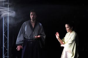 Links, Hisashi im graublauen Kimono. Er hat ein staunendes Gesicht. Rechts neben ihm steht Naoko, Sie trägt einen gelblichen Kimono und hat eine abwehrende Handgebärde.