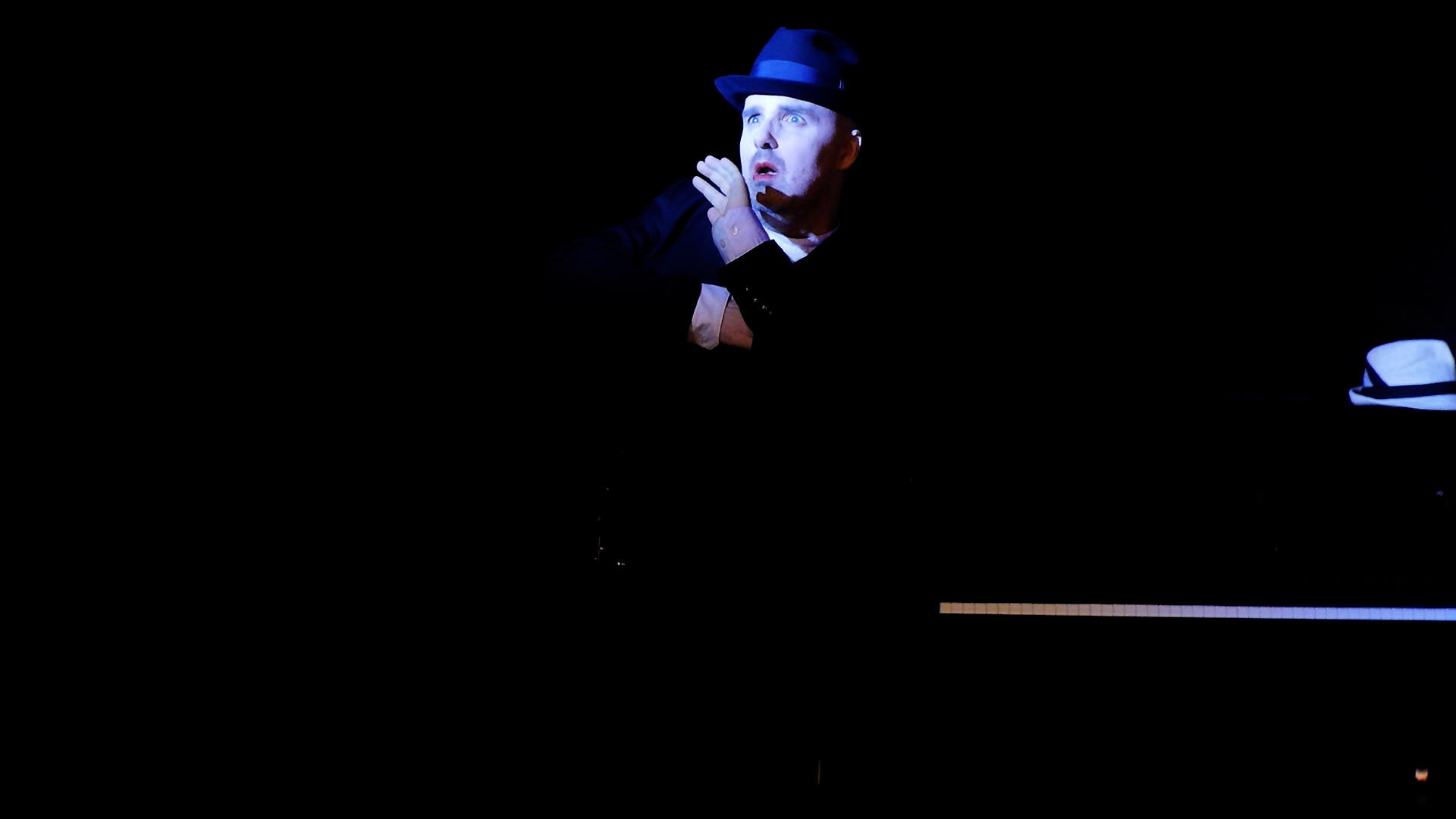 58-1024x768 Szene aus der Tor und der Tod.<br />
Der Schauspieler, der Freund, schaut nach links und fürht eine Handgebärde aus. Er trägt eien Huir uns ist dunkel gekleidewt<br />