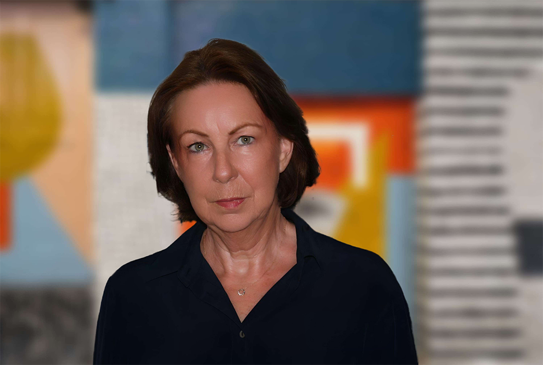 1111798_web-1024x768 Porträt der Autorin Marita Sonnenberg. Sie trägt eine dunkle Bluse und sieht konzetriert in die Kamera. sie steht vor einem hellen und buntem Hintergrund auf einer Messe.