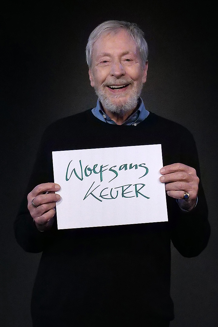 Wolfgang Keuter, 2. Vorsitzender, er trägt ein blaues Hemd und einen schwarzen Pulli und lächelt in die Kamera. In den Händen hält er eine DIN A 4 Seite auf der sein Name steht.