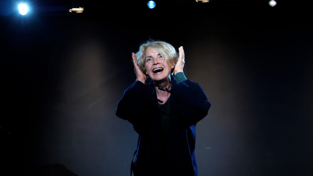 Eine junge Frau steht allein auf der Bühne des Theaterlabors Düsseldorf. Mit ruhiger, konzentrierter Körperhaltung und ernstem Blick ist sie ganz in ihre Szene vertieft und erforscht im Slow Acting Training ihre eigene Rolle und Persönlichkeit.